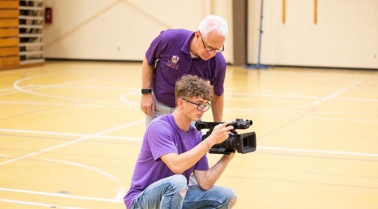 工作人员 member trains a student worker on camera operation.